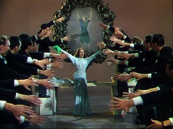Movie still from “Ziegfeld Follies” (1945), directed by Roy Del Ruth – A group of people in a circle around a woman in a blue dress; Wide shot, Low angle