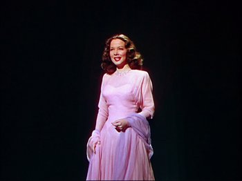 Movie still from “Ziegfeld Follies” (1945), directed by Roy Del Ruth – A woman in a pink dress standing in front of a black background; Medium shot, Low angle