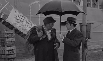 Movie still from “Zorba the Greek” (1964), directed by Michael Cacoyannis – Two men are talking under an open umbrella; Medium shot, High angle