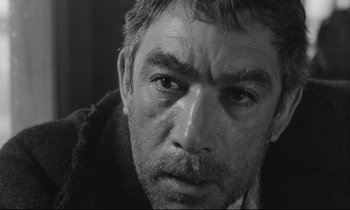 Movie still from “Zorba the Greek” (1964), directed by Michael Cacoyannis – Black and white photograph of a man looking at the camera; Close Up shot, Low angle