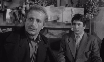 Movie still from “Zorba the Greek” (1964), directed by Michael Cacoyannis – A man and a boy are standing next to each other; Medium shot, Over the shoulder angle