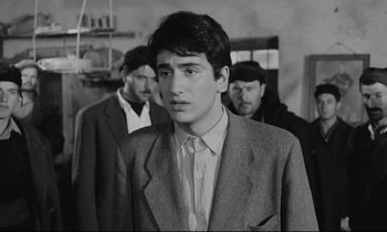 Movie still from “Zorba the Greek” (1964), directed by Michael Cacoyannis – A man in a suit and tie standing in front of two other men; Close Up shot, Over the shoulder angle