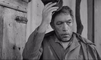 Movie still from “Zorba the Greek” (1964), directed by Michael Cacoyannis – An older man holding his hat up to his head; Close Up shot, Low angle