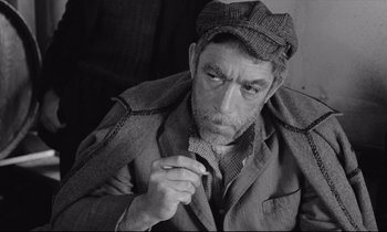 Movie still from “Zorba the Greek” (1964), directed by Michael Cacoyannis – An older man wearing a hat and smoking a cigarette; Close Up shot, High angle
