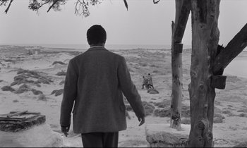 Movie still from “Zorba the Greek” (1964), directed by Michael Cacoyannis – A man walking on a beach near a body of water; Extreme Wide shot, Over the shoulder angle