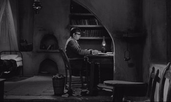 Movie still from “Zorba the Greek” (1964), directed by Michael Cacoyannis – A man sitting at a desk in front of a laptop computer; Wide shot, High angle