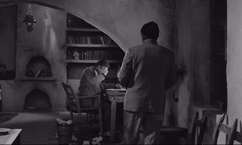 Movie still from “Zorba the Greek” (1964), directed by Michael Cacoyannis – Two men in suits are sitting at a table; Wide shot, High angle