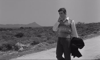 Movie still from “Zorba the Greek” (1964), directed by Michael Cacoyannis – A black and white photo of a man smoking a cigarette; Medium shot, Over the shoulder angle