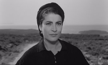 Movie still from “Zorba the Greek” (1964), directed by Michael Cacoyannis – A woman wearing a head scarf is standing in front of the ocean; Close Up shot, Low angle