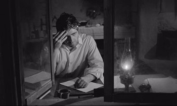 Movie still from “Zorba the Greek” (1964), directed by Michael Cacoyannis – A man sitting in front of a window looking at a paper; Medium shot, High angle