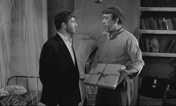 Movie still from “Zorba the Greek” (1964), directed by Michael Cacoyannis – A man holding a box talking to another man in front of him; Medium shot, Over the shoulder angle