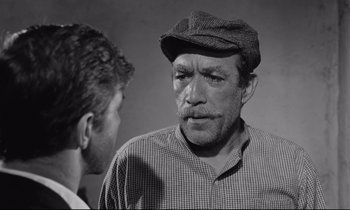 Movie still from “Zorba the Greek” (1964), directed by Michael Cacoyannis – A man in a hat and a mustache talking to another man in a plaid shirt; Close Up shot, Low angle