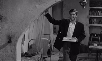 Movie still from “Zorba the Greek” (1964), directed by Michael Cacoyannis – A black and white photo of a man holding a pizza box; Medium shot, Low angle