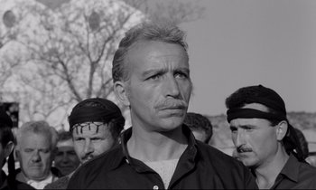 Movie still from “Zorba the Greek” (1964), directed by Michael Cacoyannis – Black and white photograph of a man in front of other men; Medium shot, Low angle