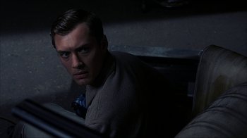 Movie still from “eXistenZ” (1999), directed by David Cronenberg – A man sitting in a chair in a dark room; Close Up shot, High angle