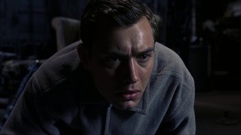 Movie still from “eXistenZ” (1999), directed by David Cronenberg – A person sitting down looking at the camera; Close Up shot, High angle