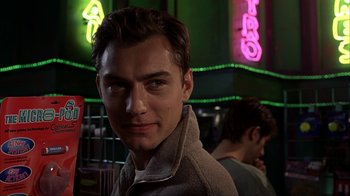 Movie still from “eXistenZ” (1999), directed by David Cronenberg – A young man is smiling for the camera in front of a neon sign; Close Up shot, Low angle