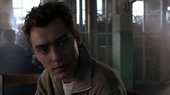Movie still from “eXistenZ” (1999), directed by David Cronenberg – A young man sitting in a room with his head turned to the side; Close Up shot, Over the shoulder angle