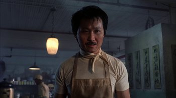 Movie still from “eXistenZ” (1999), directed by David Cronenberg – A man wearing an apron standing in a kitchen; Medium shot, Low angle