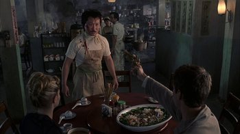 Movie still from “eXistenZ” (1999), directed by David Cronenberg – A man standing at a table with a plate of food; Medium shot, High angle