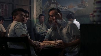 Movie still from “eXistenZ” (1999), directed by David Cronenberg – An older man holding a tray of food with a cigarette in his mouth; Medium shot, Low angle