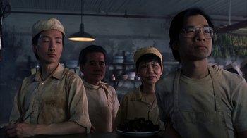 Movie still from “eXistenZ” (1999), directed by David Cronenberg – A group of people standing around a table in a kitchen; Medium shot, Low angle