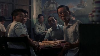 Movie still from “eXistenZ” (1999), directed by David Cronenberg – A group of men sitting around a table with sandwiches; Medium shot, High angle