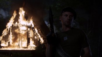 Movie still from “eXistenZ” (1999), directed by David Cronenberg – A man holding a gun in front of a fire; Medium shot, Low angle