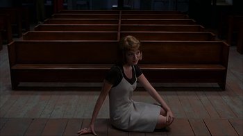 Movie still from “eXistenZ” (1999), directed by David Cronenberg – A woman sitting on the ground in front of a row of pews; Medium shot, High angle