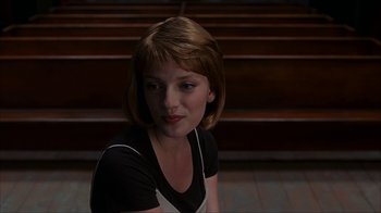 Movie still from “eXistenZ” (1999), directed by David Cronenberg – A young woman sitting on the ground in front of a wooden bench; Close Up shot, Over the shoulder angle