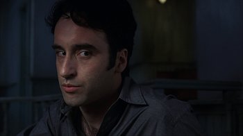 Movie still from “eXistenZ” (1999), directed by David Cronenberg – A person sitting in a room; Close Up shot, Low angle