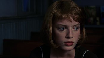 Movie still from “eXistenZ” (1999), directed by David Cronenberg – A woman with short brown hair sitting in a dark room; Close Up shot, Over the shoulder angle