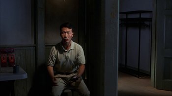 Movie still from “eXistenZ” (1999), directed by David Cronenberg – A man sitting on a chair in a dark room; Medium shot, High angle