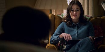 Movie still from “Archive 81” (2022), created by Rebecca Sonnenshine – A woman sitting in a chair holding a tablet; Medium shot, Over the shoulder angle