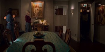 Movie still from “Archive 81” (2022), created by Rebecca Sonnenshine – A woman sitting at a dining room table in front of a painting; Wide shot, Over the shoulder angle