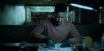 Movie still from “Archive 81” (2022), created by Rebecca Sonnenshine – A man in a red sweater is working on a piece of paper; Medium shot, Low angle