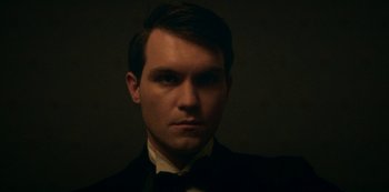 Movie still from “Archive 81” (2022), created by Rebecca Sonnenshine – A person wearing a suit and bow tie; Close Up shot, Low angle