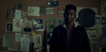 Movie still from “Archive 81” (2022), created by Rebecca Sonnenshine – A man standing in front of a wall covered with pictures; Medium shot, Over the shoulder angle