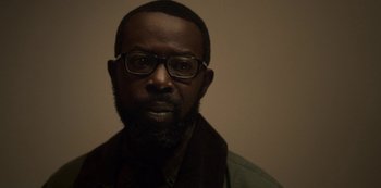 Movie still from “Archive 81” (2022), created by Rebecca Sonnenshine – A person with a beard wearing glasses; Close Up shot, Low angle