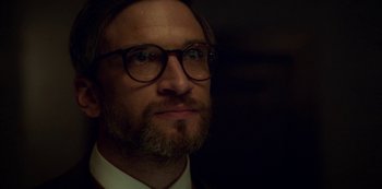 Movie still from “Archive 81” (2022), created by Rebecca Sonnenshine – A person wearing glasses and a suit; Close Up shot, Low angle