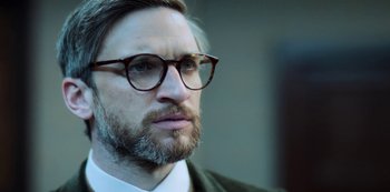 Movie still from “Archive 81” (2022), created by Rebecca Sonnenshine – A person wearing glasses and a suit; Close Up shot, Over the shoulder angle