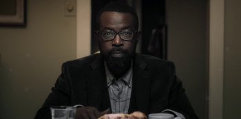 Movie still from “Archive 81” (2022), created by Rebecca Sonnenshine – A man sitting at a table with a plate in front of him; Close Up shot, Over the shoulder angle