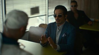 Movie still from “Army of the Dead” (2021), directed by Zack Snyder – A man in a suit and sunglasses sitting at a table; Medium shot, Over the shoulder angle