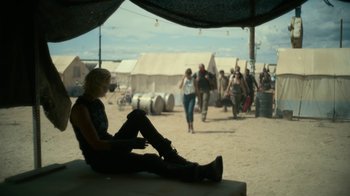 Movie still from “Army of the Dead” (2021), directed by Zack Snyder – A woman sitting on the side of the road in front of tents; Wide shot, Over the shoulder angle
