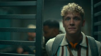 Movie still from “Army of the Dead” (2021), directed by Zack Snyder – A man with blonde curly hair is standing next to a window; Close Up shot, Low angle