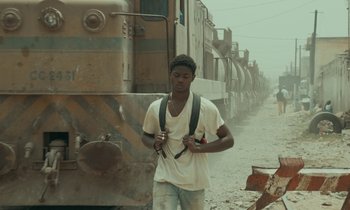 Movie still from “Atlantics” (2019), directed by Mati Diop – A man standing in front of a train on the tracks; Medium shot, Low angle