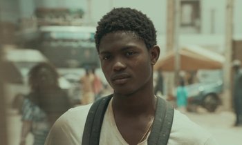 Movie still from “Atlantics” (2019), directed by Mati Diop – A young man with a beard is standing in a street; Close Up shot, Over the shoulder angle