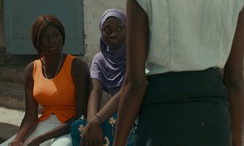 Movie still from “Atlantics” (2019), directed by Mati Diop – A group of women sitting next to each other on a couch; Medium shot, Over the shoulder angle