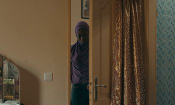 Movie still from “Atlantics” (2019), directed by Mati Diop – A woman standing in front of an open door; Medium shot, Over the shoulder angle