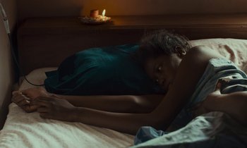 Movie still from “Atlantics” (2019), directed by Mati Diop – A person laying on a bed with a candle in the background; Medium shot, High angle